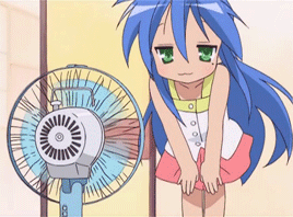 a moving gif of konata izumi from the anime lucky star standing in front of a desk fan. her hair is being blown around.